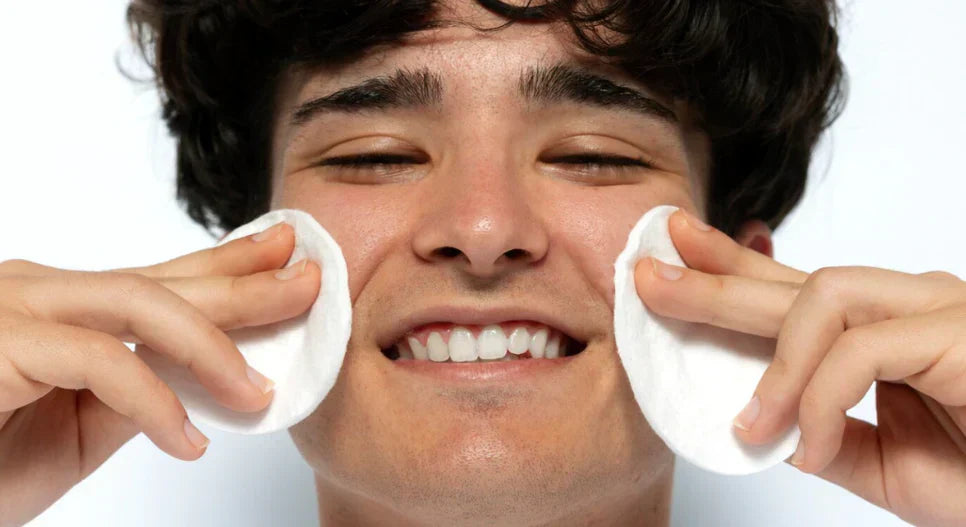Man smiling while using cotton pads for skincare, referencing Double Cleansing for Men: Is it really necessary if you don't wear makeup?