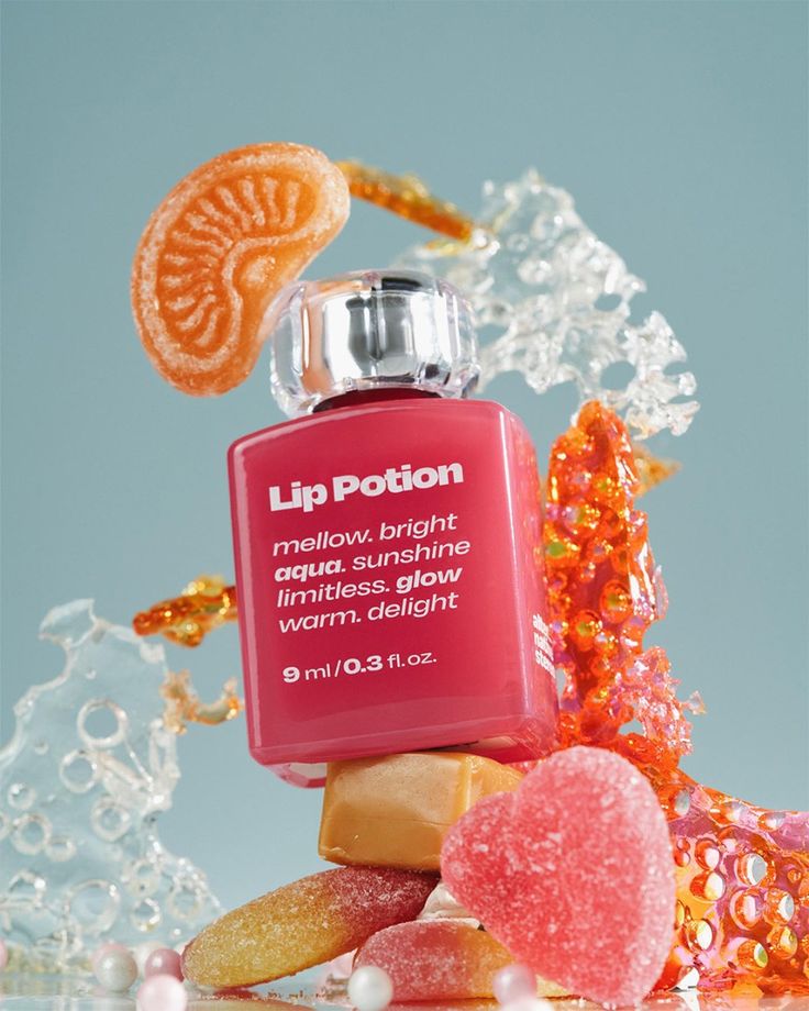 Lip Potion beauty product surrounded by colorful candy and sugar art against a blue background, highlighting glow and delight attributes.