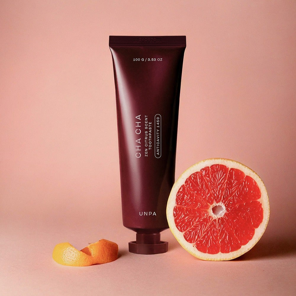 UNPA Cha Cha Zen Grapfruit Scent 1450 High Fluoride Toothpaste 100g tube with sliced grapefruit on a pink background
