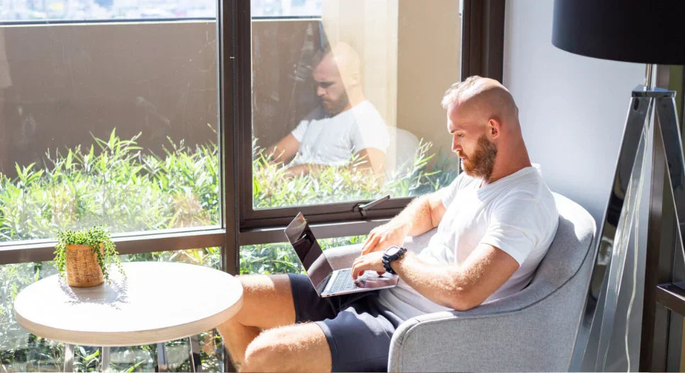 Sunscreen Indoors? Why your office lights are aging your skin - man working on laptop near window with sunlight exposure