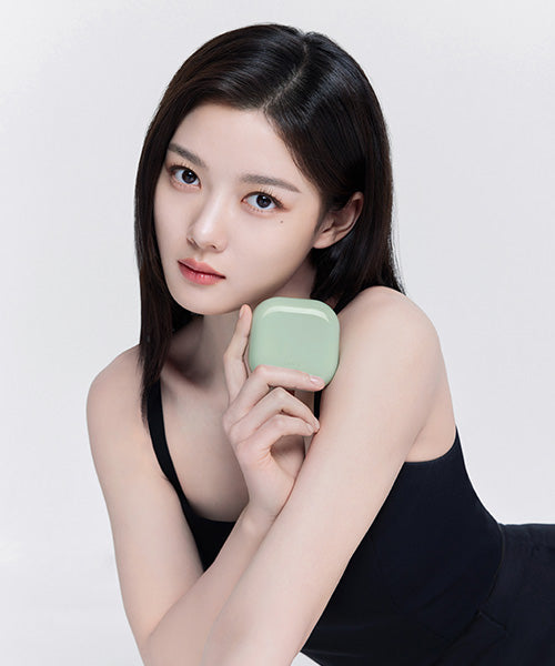 Person holding a green compact case, posing in a black outfit against a plain background.