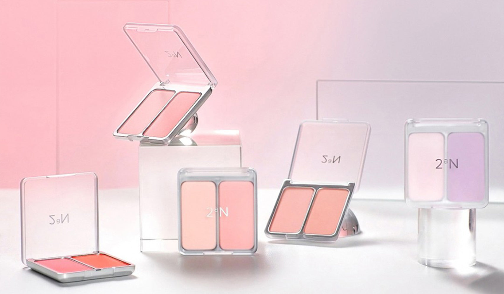 Assorted blush and makeup palettes on display against a pink backdrop, featuring various shades in sleek packaging.