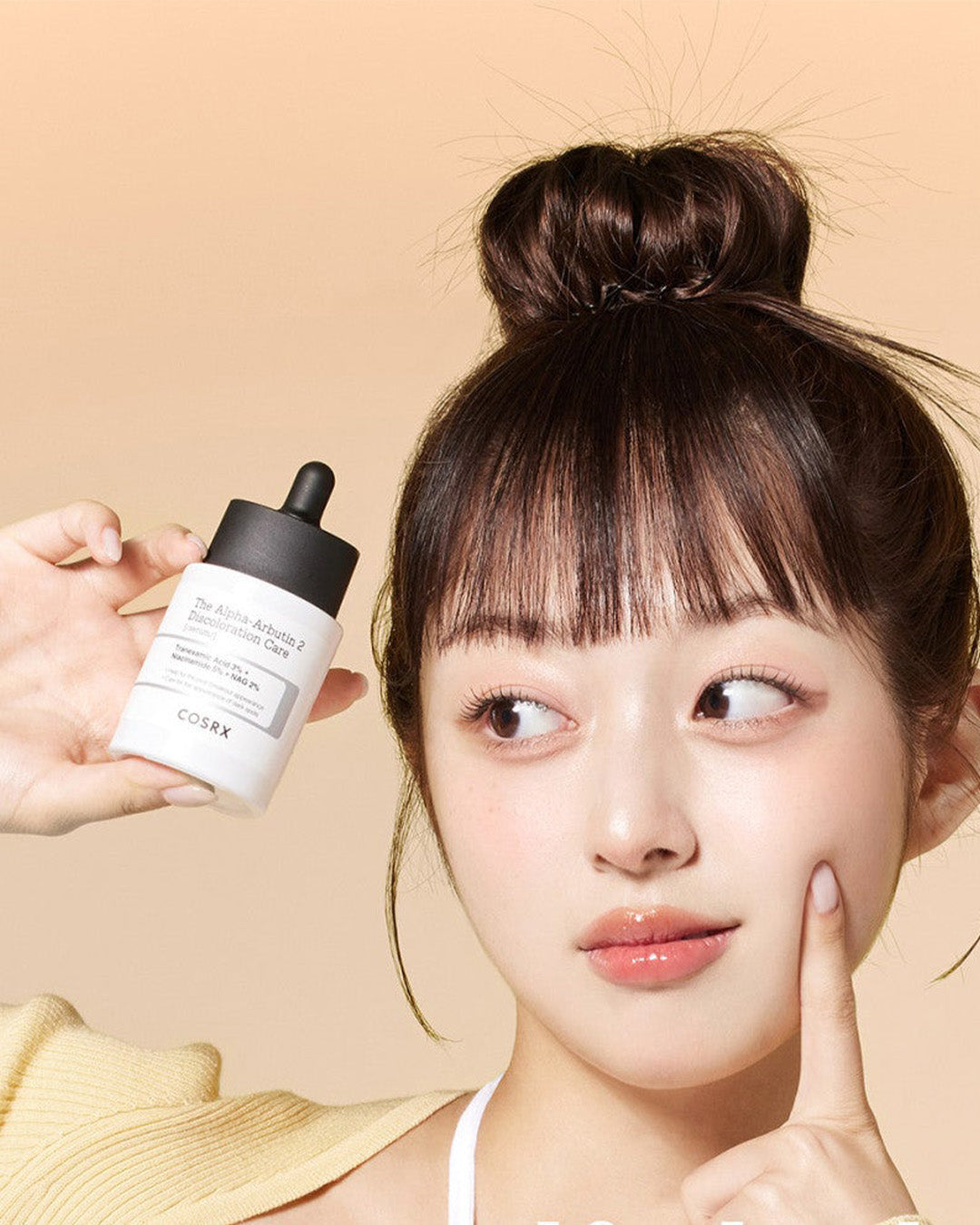 Person holding a bottle of facial serum against a neutral background, highlighting skincare routine.