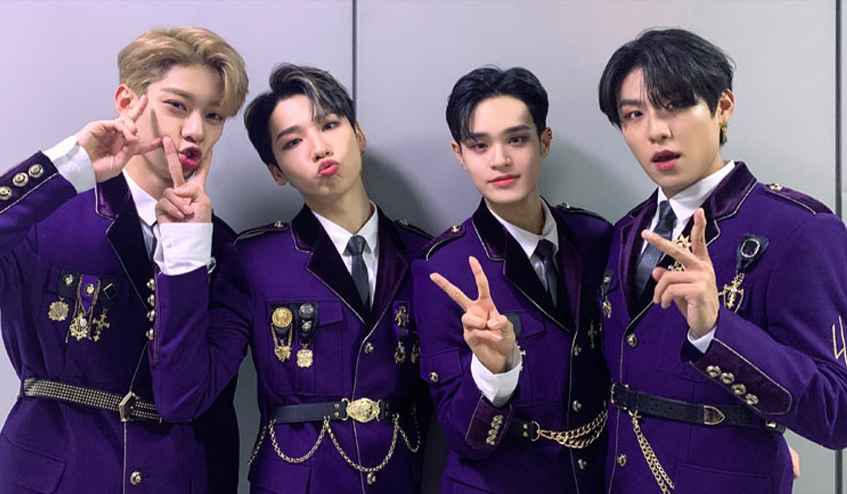 Four young men posing in matching purple outfits with peace signs and playful expressions.