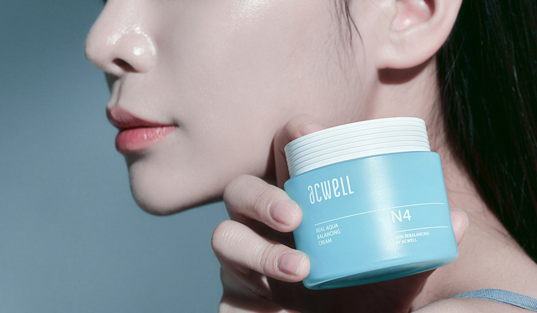 Close-up of a woman holding a jar of ACWELL Aqua Balm lotion highlighting skincare and hydration benefits.