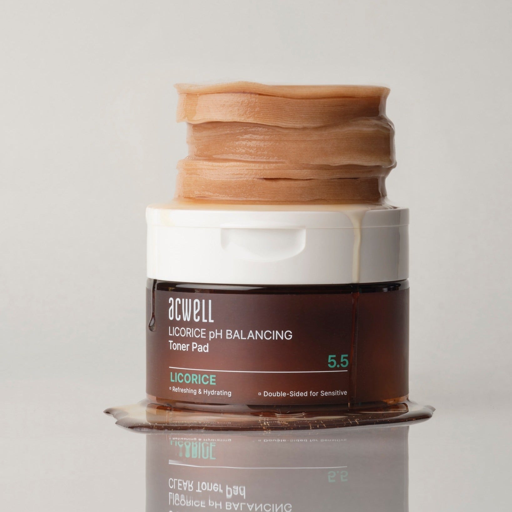 ACWELL Licorice pH Balancing Toner Pad 70P container with stack of pads and spilled liquid on reflective surface, front view.