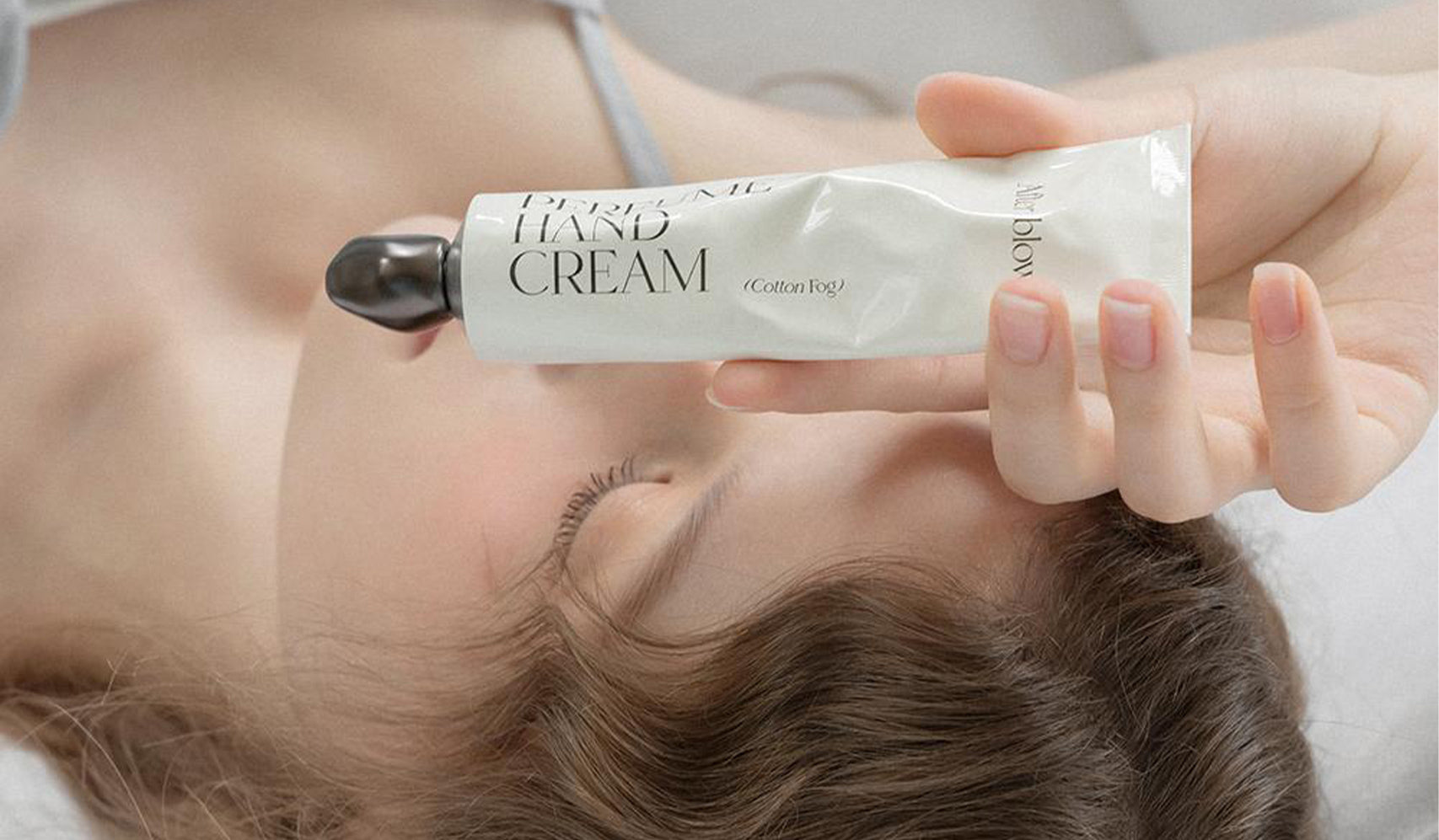 Person holding a tube of hand cream while lying down, focusing on skincare and relaxation.