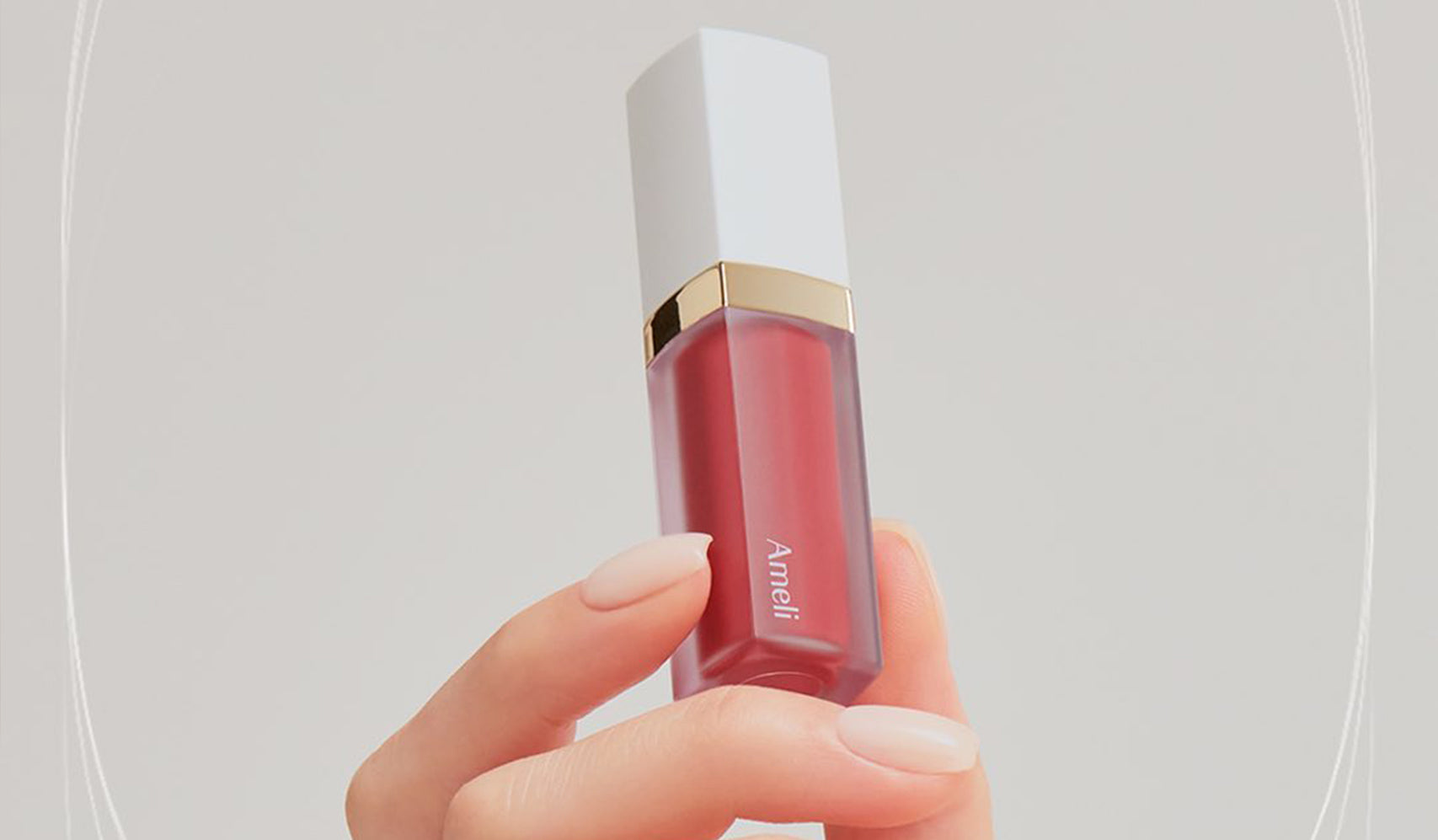 Hand holding a luxury red lipstick tube with white cap against neutral background