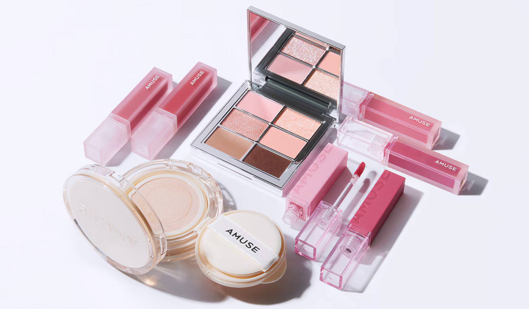Amuse makeup set with eyeshadows, lip glosses, and compact powders arranged on a white surface.