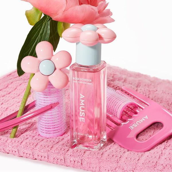 AMUSE Rose Powder Hair Perfume Mist 30ml with pink flower cap and styling accessories on a pink background.