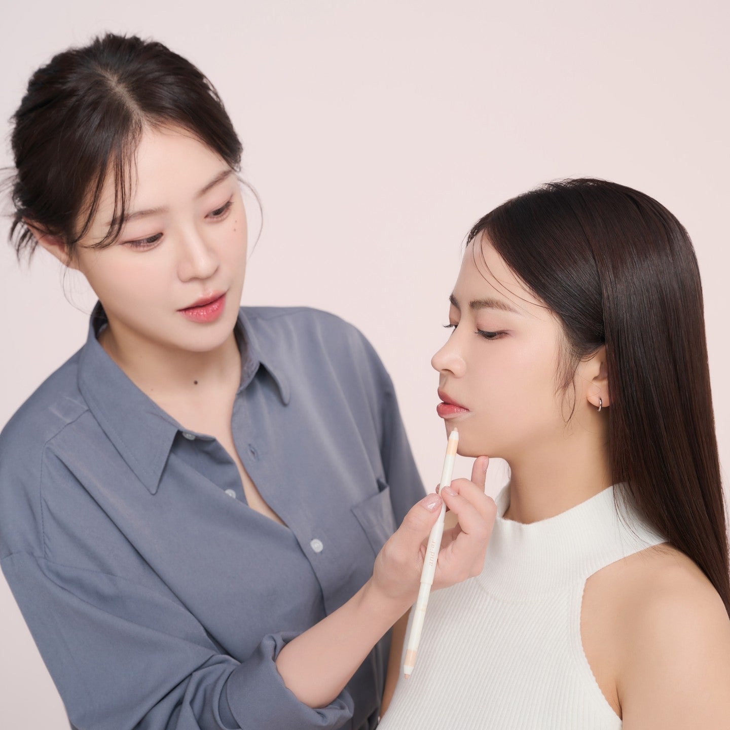 Makeup artist applying AND:AR Soft Skinfit Dual Concealer Pencil on a model's face, showcasing its application and coverage.