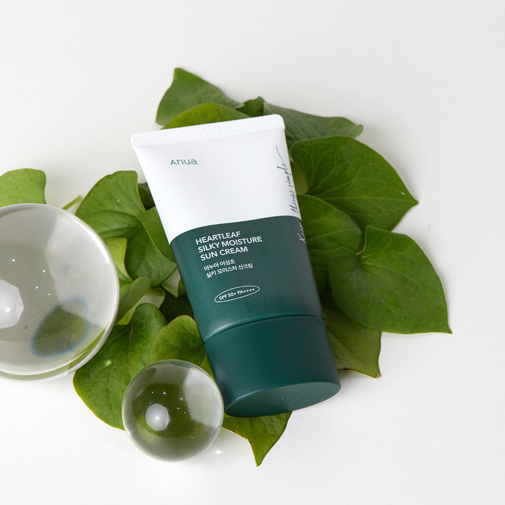 ANUA Heartleaf Silky Moisture Sun Cream 50ml displayed with green leaves and glass decor for skincare and sun protection.