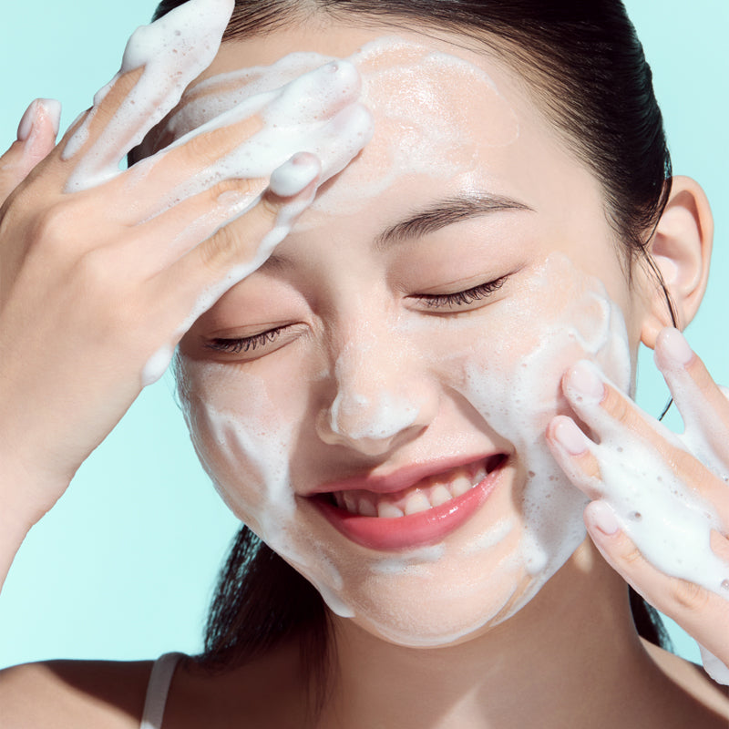 Woman using ANUA PDRN Hyaluronic Acid Moisture Cleansing Foam 150ml on face, smiling as she applies foam for skincare routine