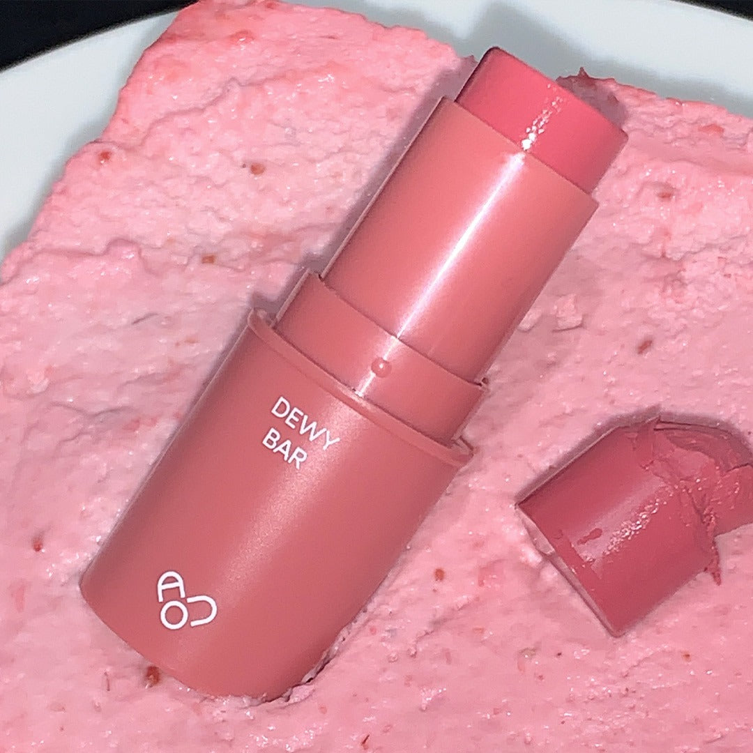 AOU Dewy Bar on textured pink background, highlighting its creamy finish and vibrant color.