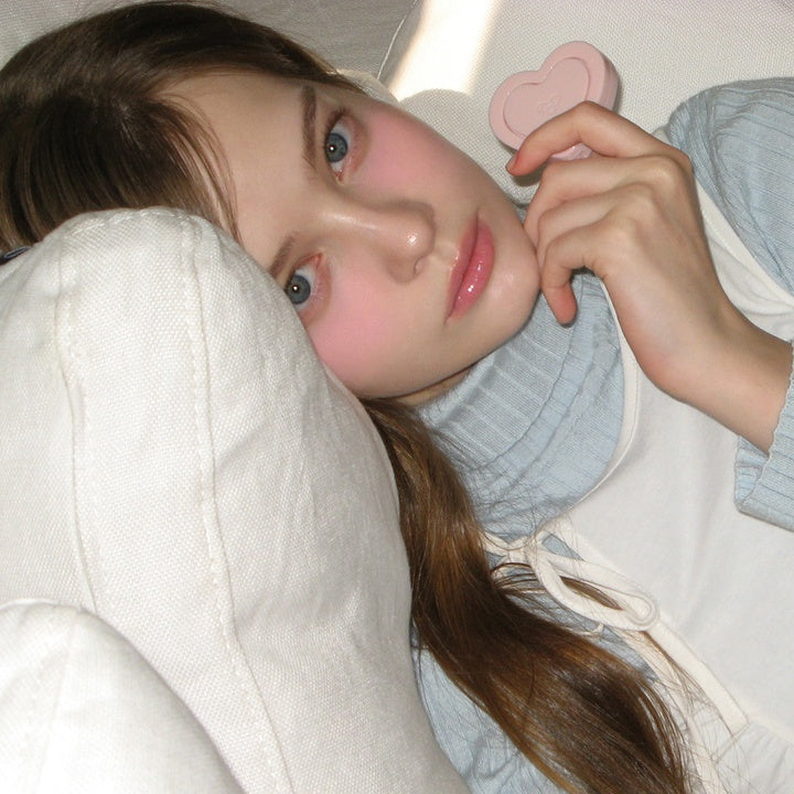 Person holding AOU Soft Cream Blush, showcasing soft pink tones on cheeks, enhancing natural beauty with gentle makeup look.