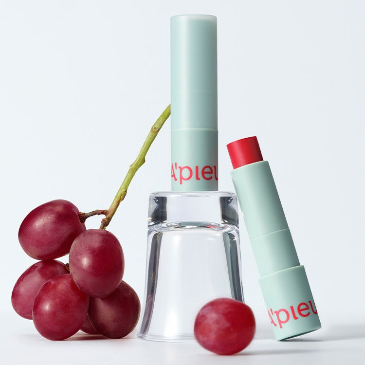 A'PIEU Juicy Pang Care Lip Balm next to fresh grapes for nourishing lip care.