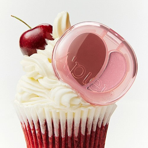 A'PIEU Juicy Pang Mood Blending Lip & Cheek Balm displayed with cherry cupcake background