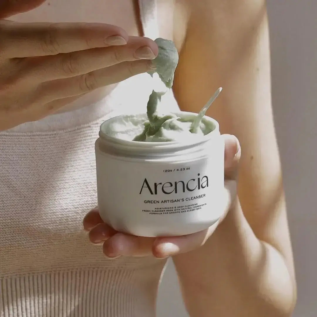 Person holding open jar of ARENCIA Green Artisan Skin Boosting Cleanser 120g with a spatula scooping product.