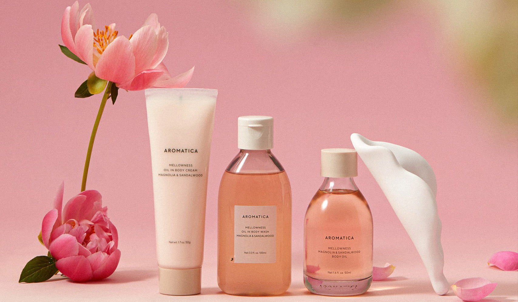 Aromatica skincare products with pink flowers and petals on a pink background