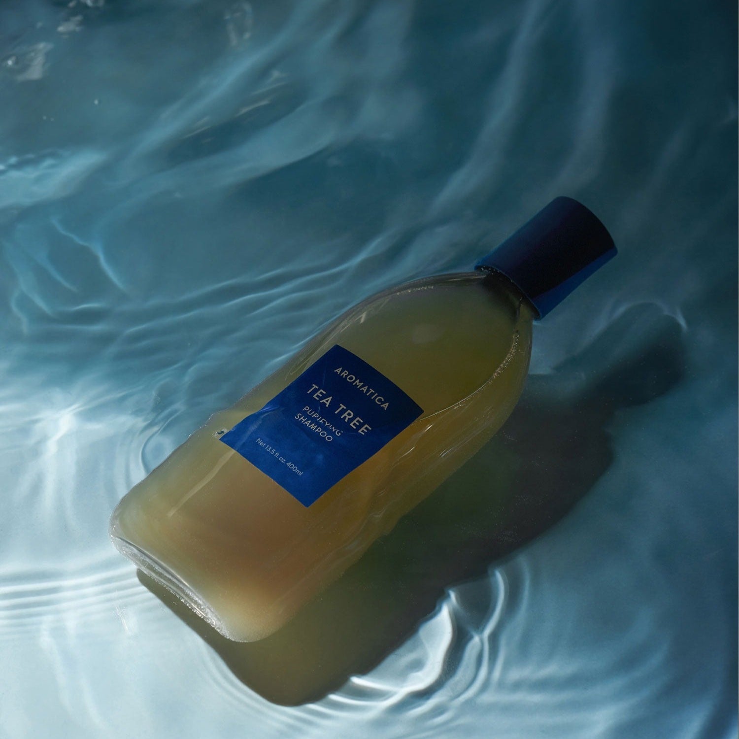 AROMATICA Tea Tree Purifying Shampoo 750ML bottle in calming water setting, promoting a refreshing and cleansing hair care experience