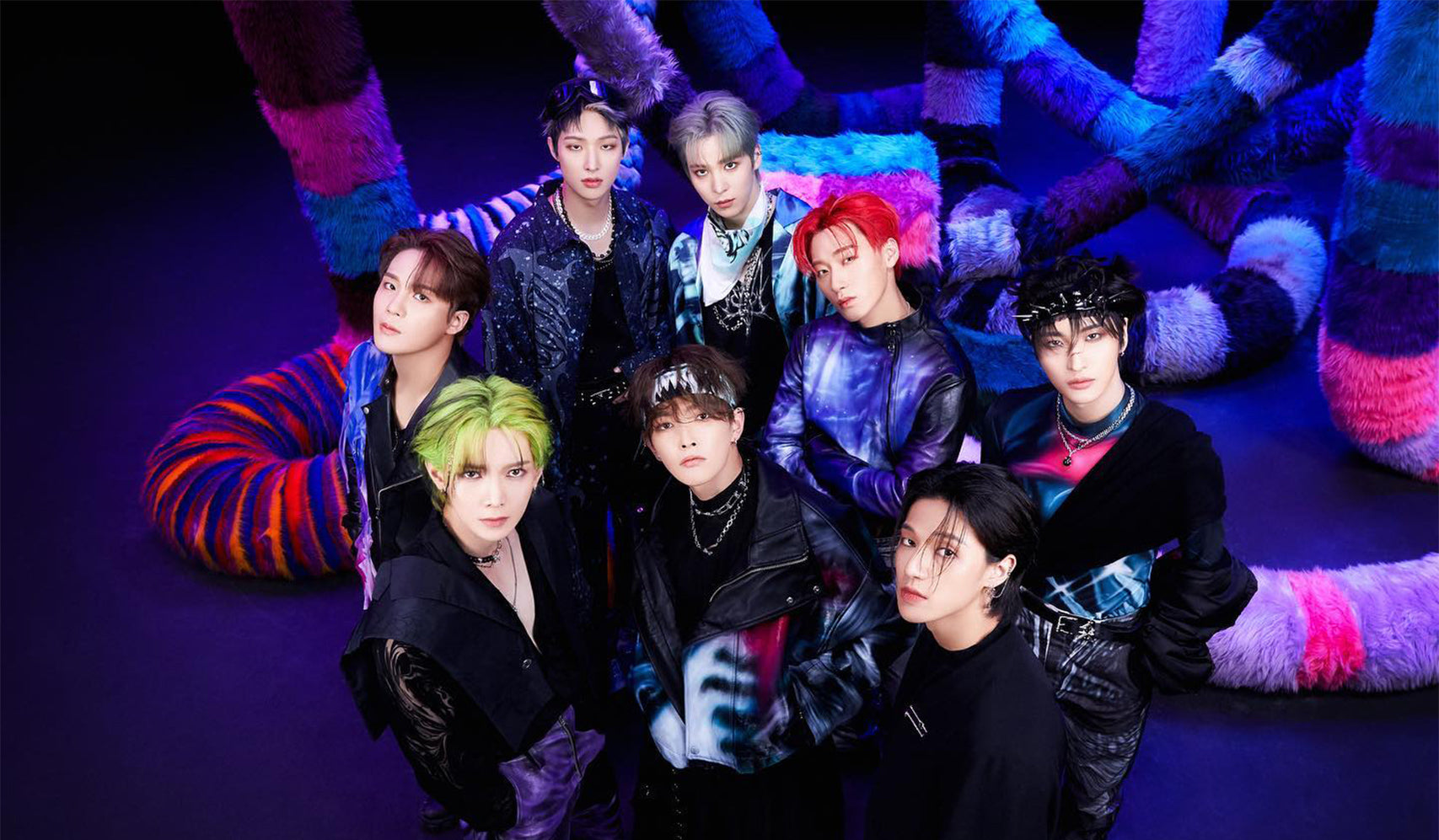 Colorful group of eight performers posing on stage with vibrant, twisted decorations in the background.