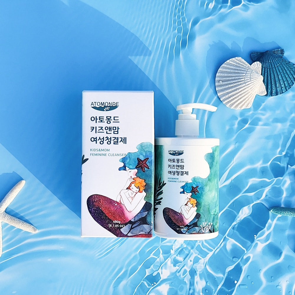 Bottle and box of ATOMANDE Kids & Mom Feminine Cleanser 400g placed on a watery background with sea shells.