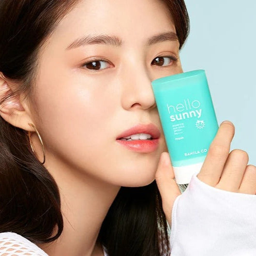 Close-up of model with BANILACO Hello Sunny Essence Sun Stick Fresh SPF50+PA++++ in hand, showcasing skincare product.