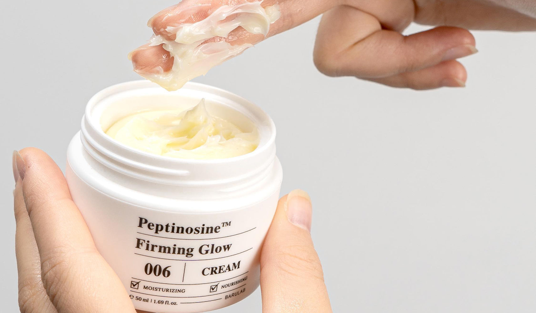 Person applying Peptinosine Firming Glow cream from a white jar with a finger swatch, showcasing texture of the skincare product.