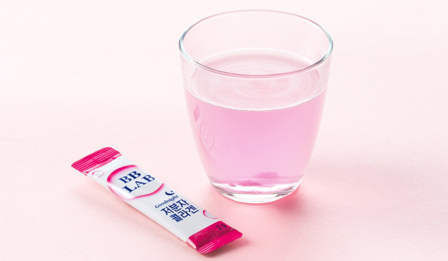 Glass of pink drink next to BB LAB supplement stick on pastel background