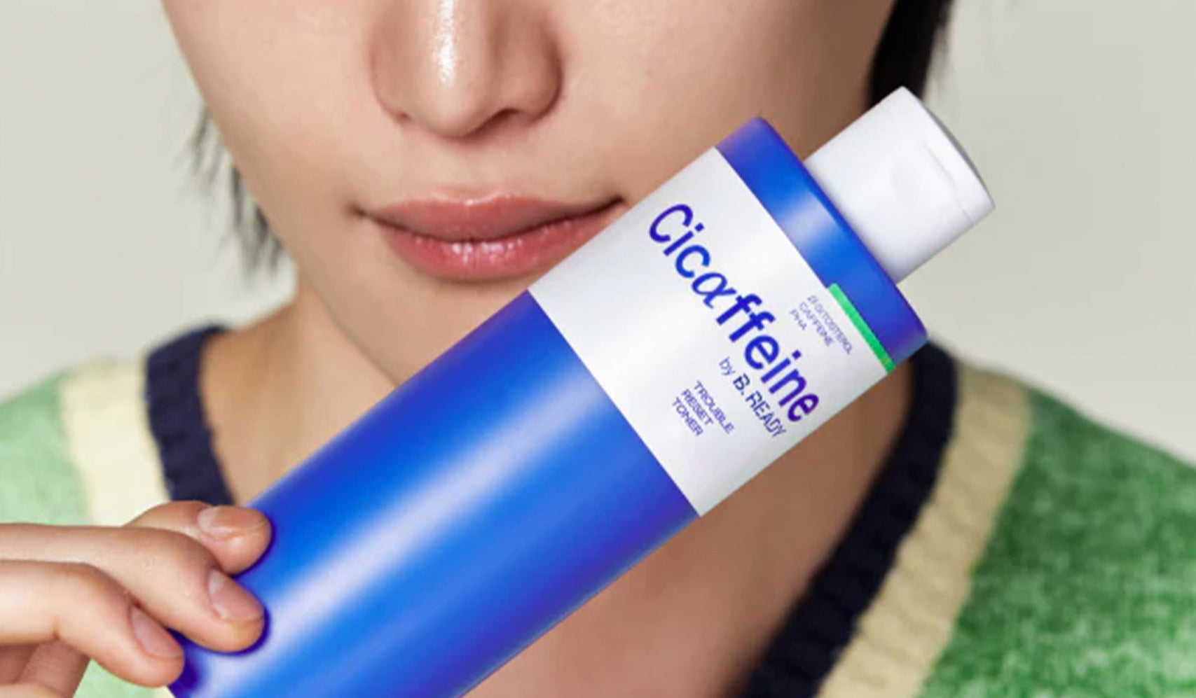 Close-up of a person holding a blue bottle labeled 'Cicaffeine' by some by mi, showcasing skincare product packaging.