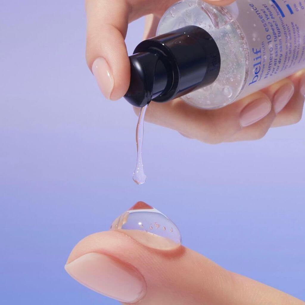Person dispensing BELIF Numero 10 Essence 125ml onto finger, showcasing texture and consistency of skincare product.