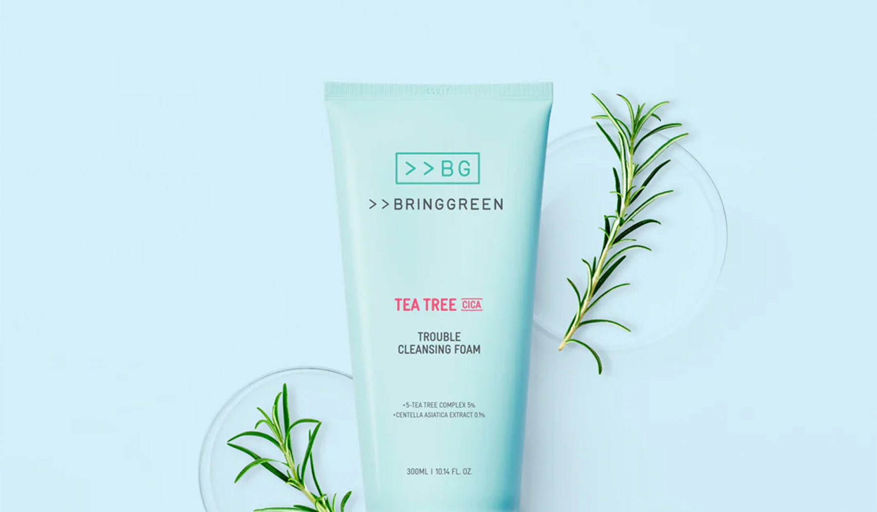 Bringgreen Tea Tree Trouble Cleansing Foam tube surrounded by green rosemary sprigs on a light background.
