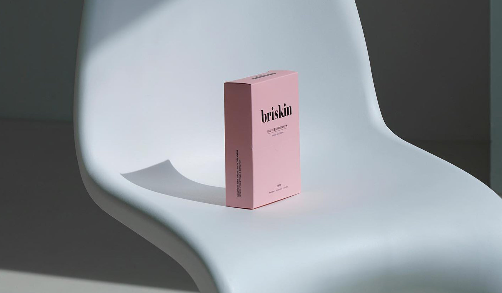 Briskin skincare product box on a modern white chair in minimalistic setting.