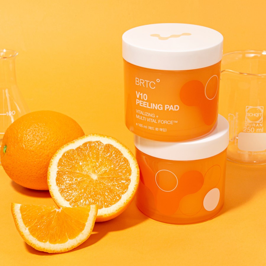 BRTC V10 Peeling Pad 80pcs 165ml displayed with fresh oranges and laboratory beakers on an orange background