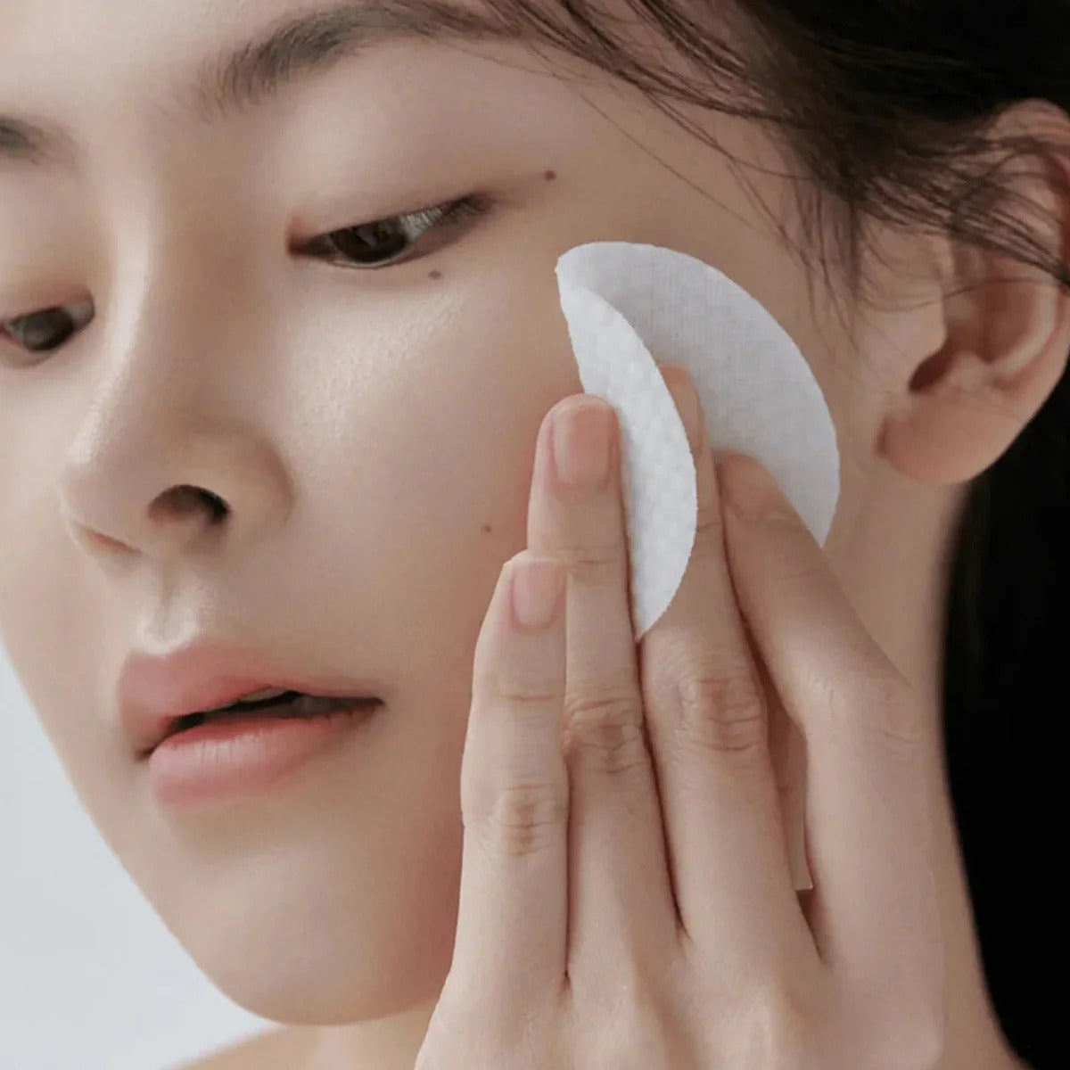 Woman using CELIMAX Ji Woo Gae Heartleaf BHA Peeling Pad 60 Pads on face, showcasing product effectiveness and gentle exfoliation.