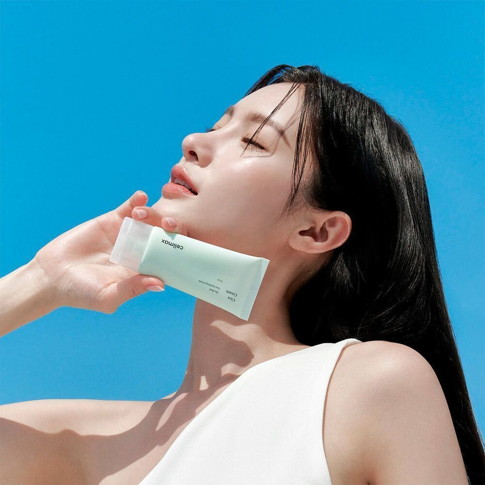Woman holding CELIMAX The Real Cica Soothing Cream 50ml against a blue sky