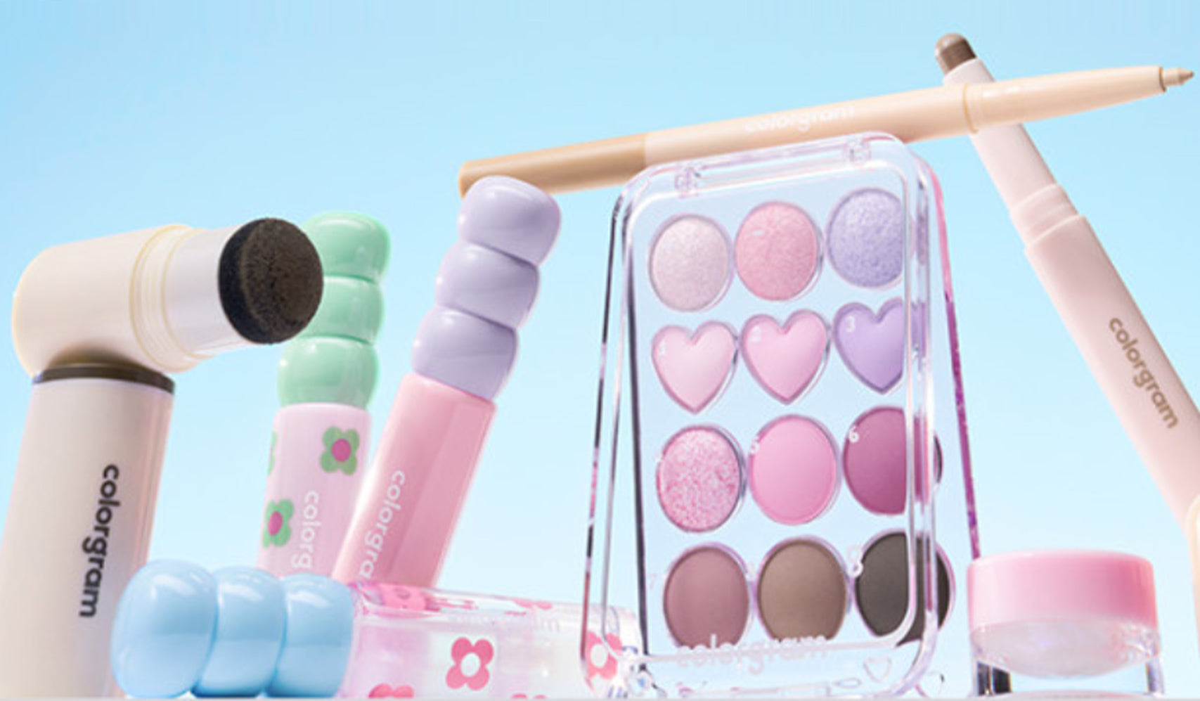 Pastel-themed makeup set with eyeshadow palette and cosmetics on a blue background.