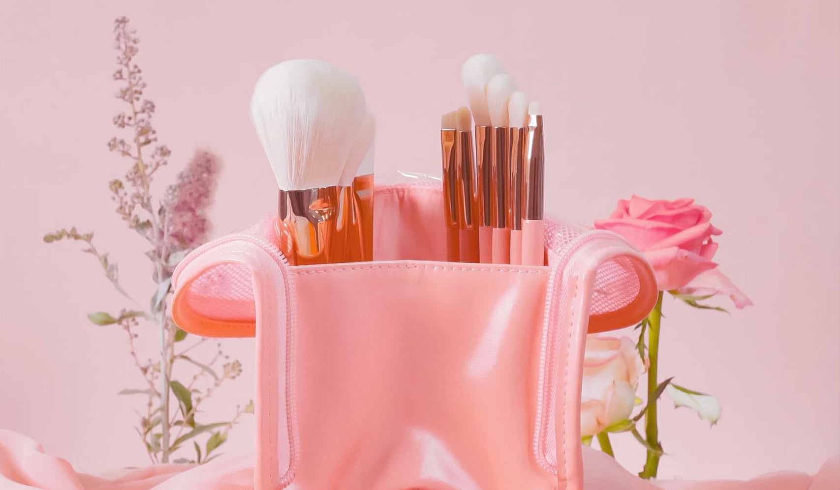 Pink makeup bag with brushes and flowers in the background