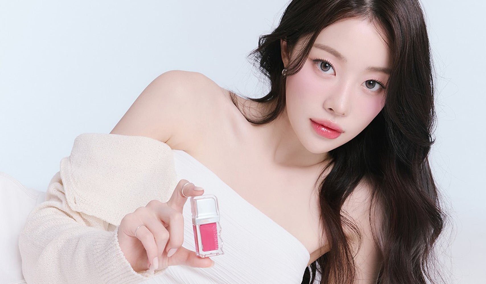 Woman showcasing makeup product in elegant portrait.