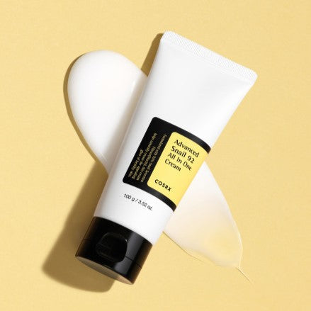 COSRX Advanced Snail 92 All In One Cream 100g tube on a yellow background, highlighting skincare benefits and packaging design.