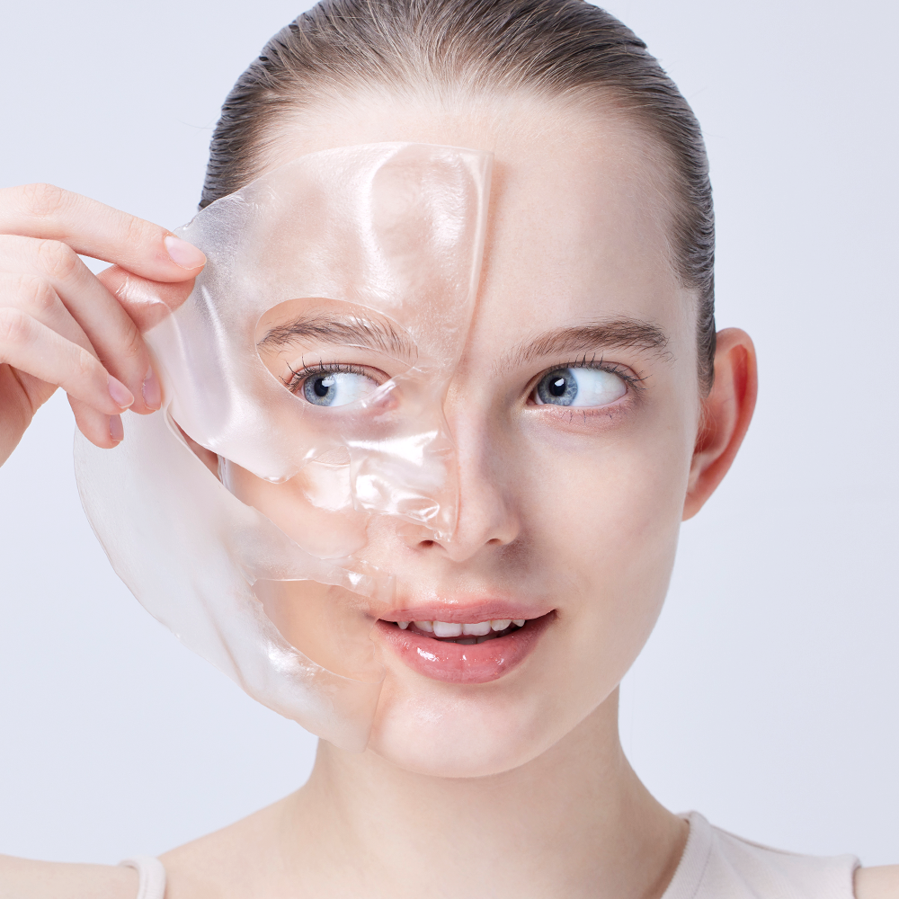 Woman applying COSRX The Alpha-Arbutin Discoloration Care Hydrogel Mask (3EA) to her face, showing skincare application process.