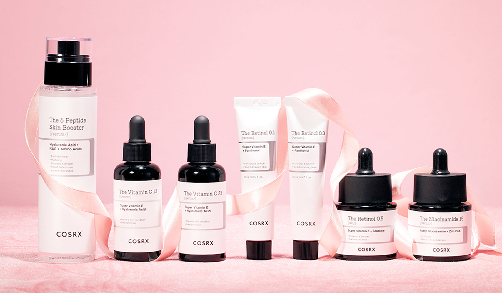 Cosmetic skincare products including serums and creams on a pink background. Products wrapped with a ribbon.