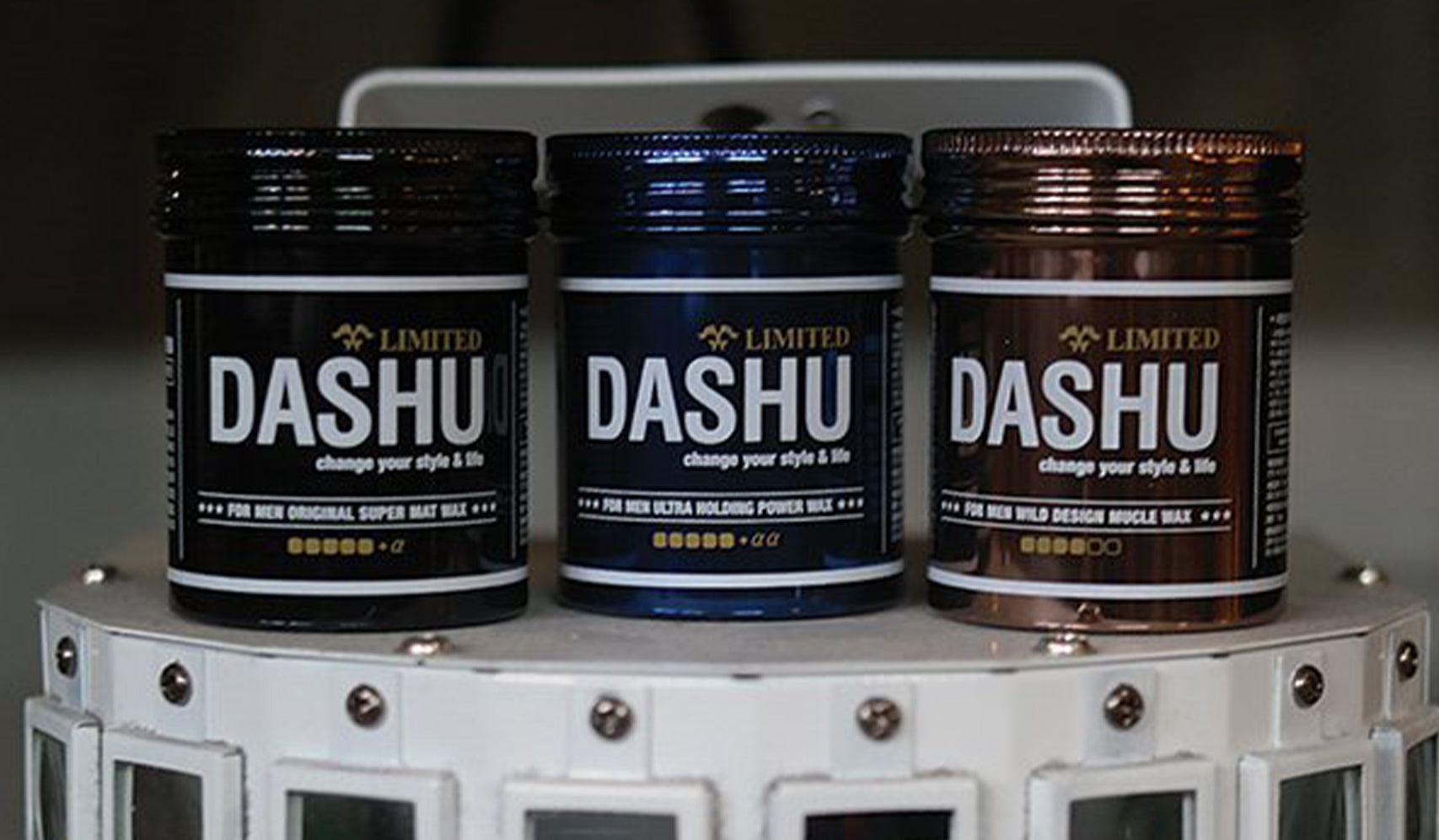 Three containers of Dashu hair styling pomade in different colors displayed on a white surface.