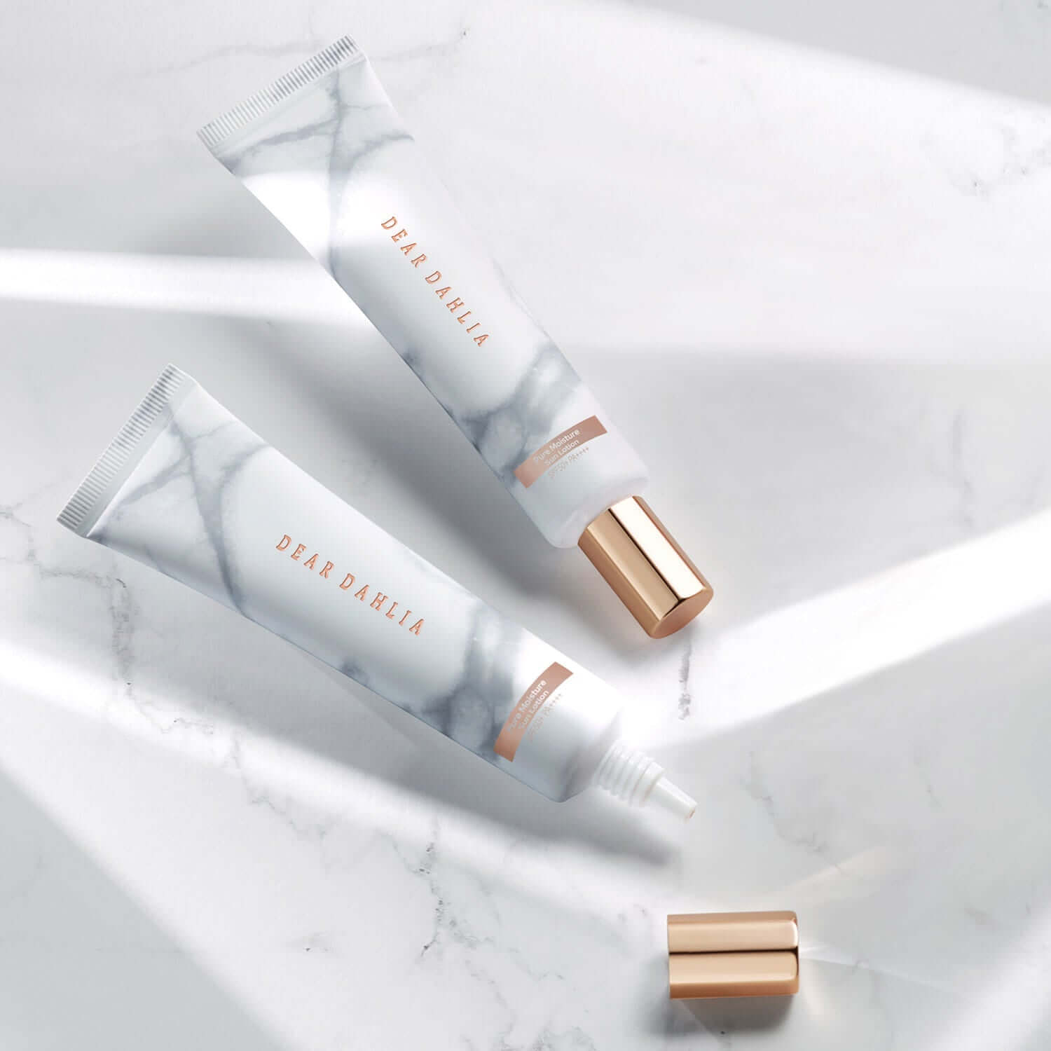 DEAR DAHLIA Skin Paradise Pure Moisture Sun Lotion on marble surface with rose gold caps.