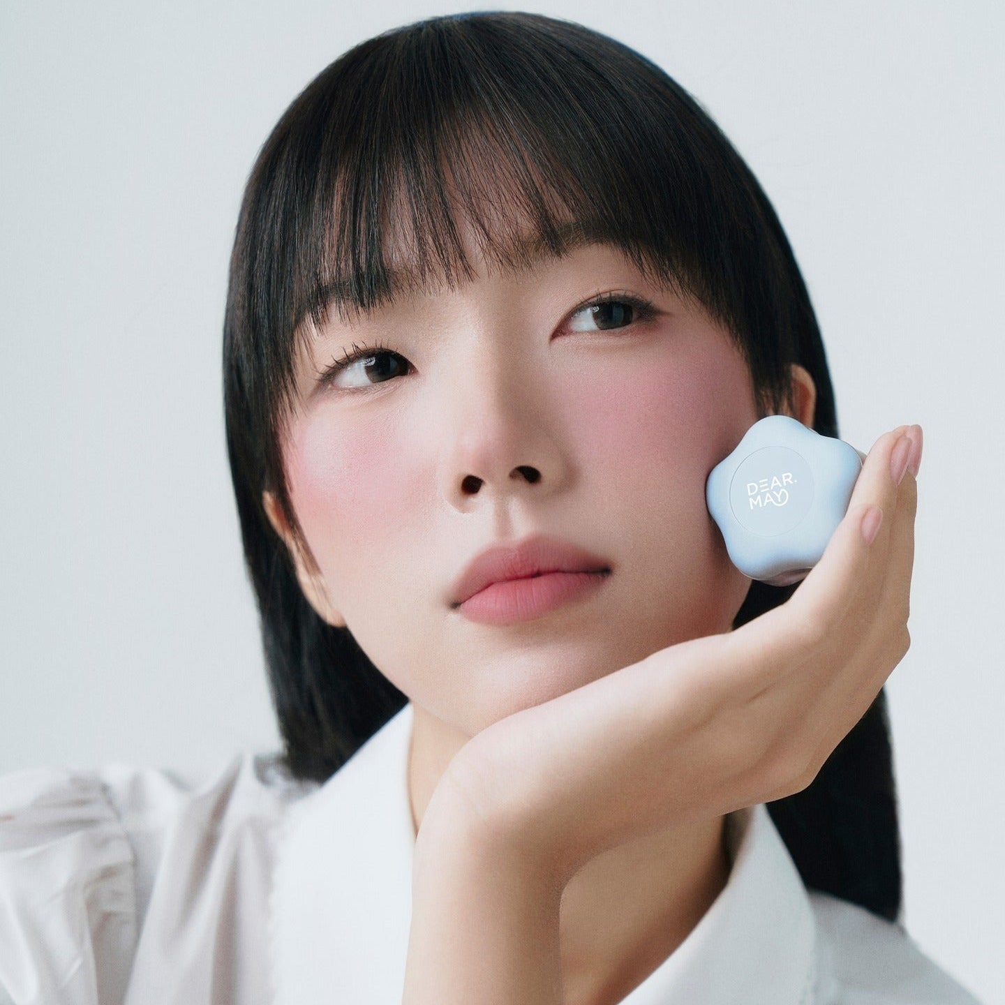 Person holding DEAR MAY Pure Falling Mood Lip Pot 6.5g with soft pink lips and rosy cheeks, showcasing makeup beauty.