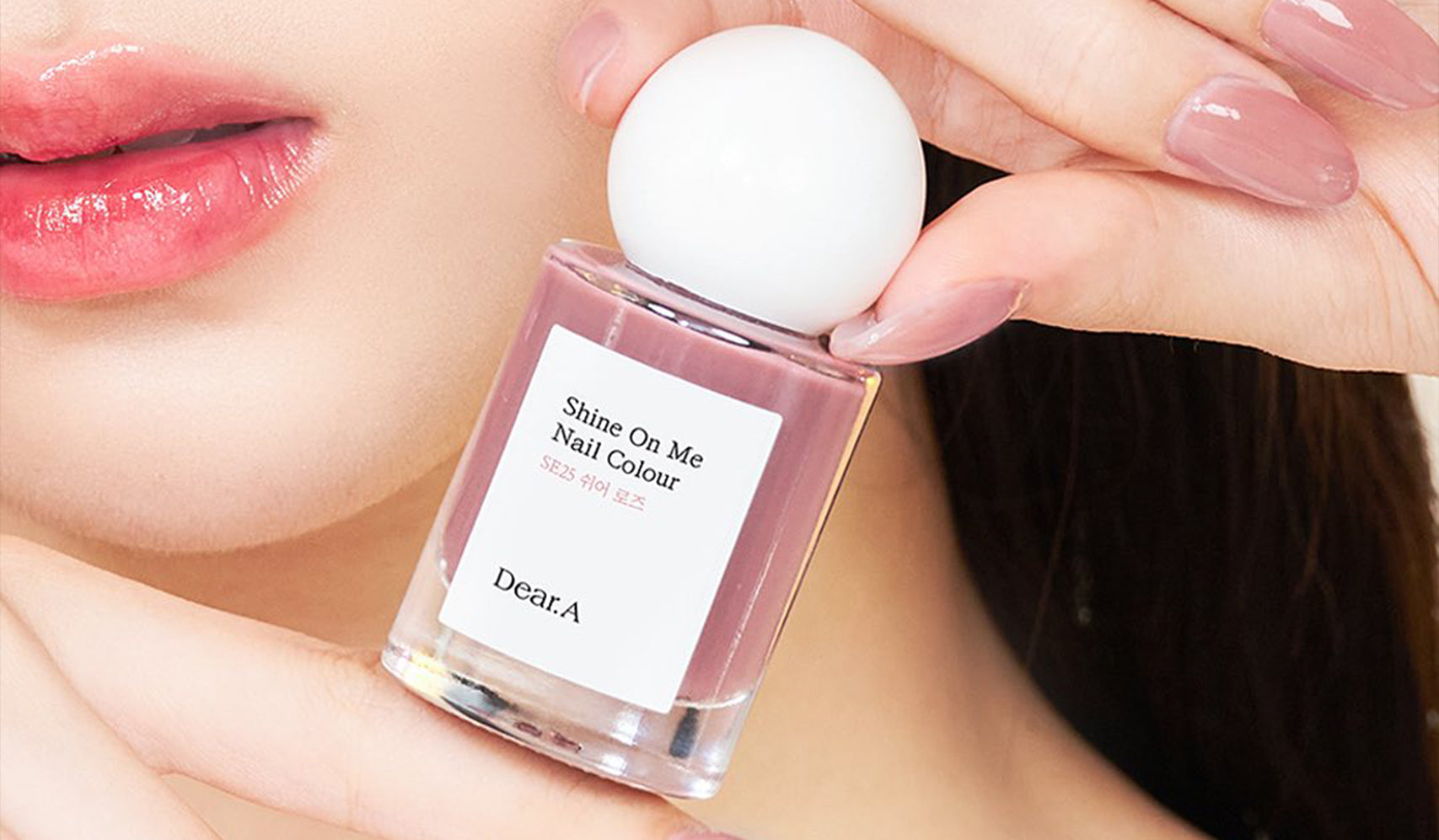 Close-up of hands holding a bottle of 'Shine On Me' nail polish by Dear.A, showcasing glossy pink nails and product design.