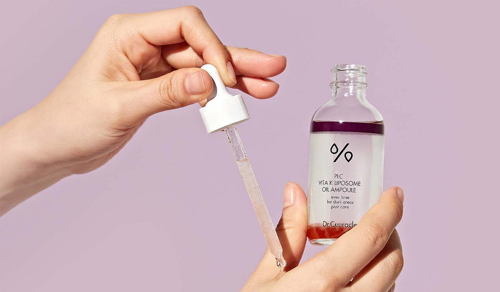Person holding a bottle of serum with a dropper against a light purple background, showcasing skincare product application.