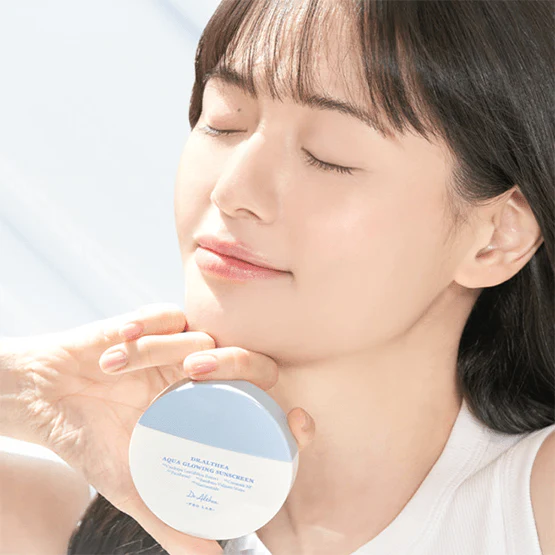 Woman holding DR.ALTHEA Aqua Glowing Sunscreen 45ml, enjoying sunlight with closed eyes, showcasing the product's skincare benefits.