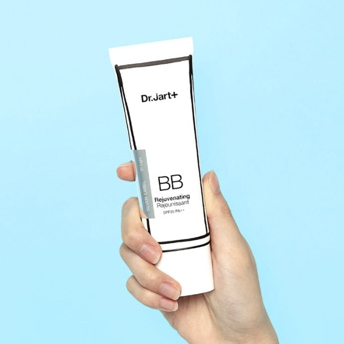 Hand holding DR.JART+ BB Rejuvenating 50ml tube against blue background