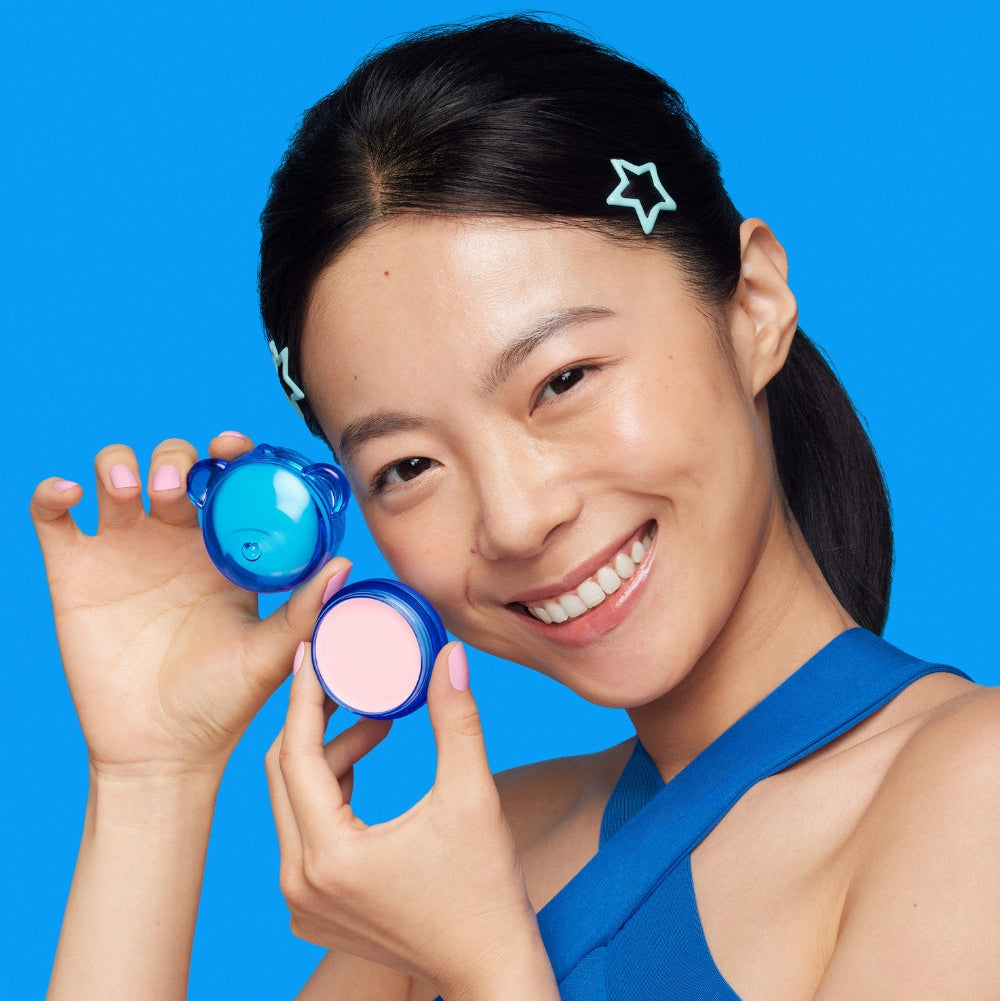 Person holding DR.JART+ Vital Hydra Solutionâ„¢ Hydrating Lip Mask with a smile on a blue background.